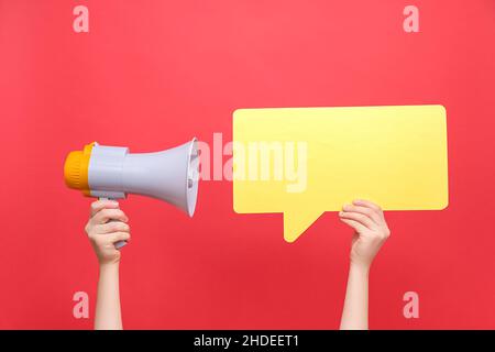 Nahaufnahme von weiblichen Händen, die eine leere, gelbe Sprechblase aus Papier und ein Megaphon halten, isoliert über einem pastellroten Hintergrund-Studio mit Kopierraum für Sie Stockfoto