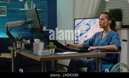 Ungültiger Fotograf, der im Studio mit einem Grafiktablett und einem Stylus am Computer arbeitet. Fotokünstler mit Handicap, der Bilder auf dem Touchscreen retuschierte und im Rollstuhl saß. Stockfoto