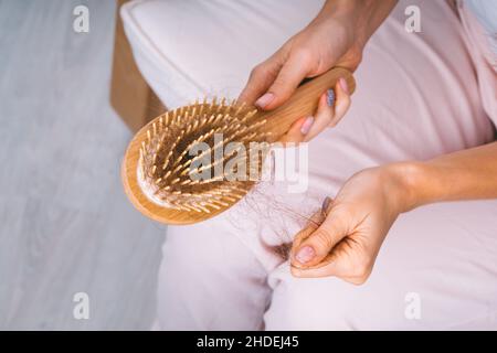 Frau, die ihr Haar aus der Haarbürste nimmt. Haarausfall Problem. Schlechte Haare fallen heraus Stockfoto