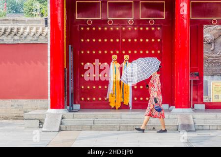 XI'AN, CHINA - 5. AUGUST 2018: Frau mit Regenschirm passiert vor dem Guangren Lama Tempel in Xi'an, China Stockfoto