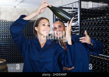 Männer und Frauen, die im Weinkeller stehen und dabei den Sekt in der Flasche betrachten Stockfoto