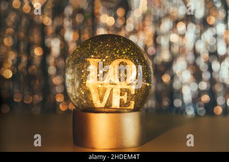 Valentinstag Hintergrund. Glitzer-Globus mit WORTLIEBE auf dem goldglänzenden Bokeh-Hintergrund. Selektiver Fokus. Speicherplatz kopieren Stockfoto