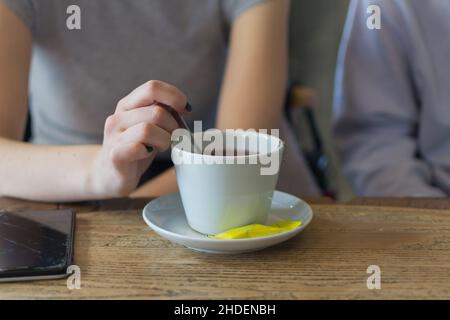 Dame, die in einem Café in Novi Sad, Serbien, eine Tasse Tee mit Zucker auf einem Holztisch trinkt Stockfoto