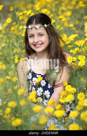 Junge 11 Jahre alte Mädchen in floralen Sommerkleid in einem Feld von gelben wilden Gänseblümchen Stockfoto