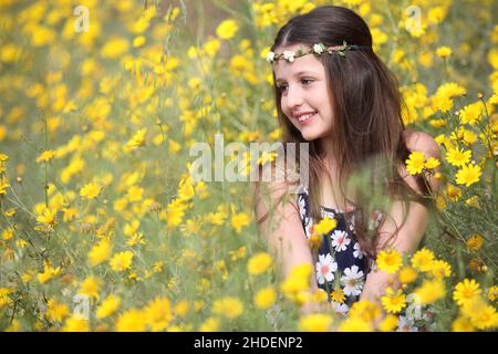 Junge 11 Jahre alte Mädchen in floralen Sommerkleid in einem Feld von gelben wilden Gänseblümchen Stockfoto