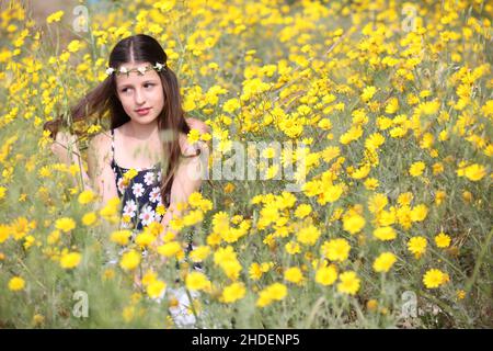 Nachdenklich Junges 11 Jahre altes Mädchen in floralem Sommerkleid in einem Feld von gelben wilden Gänseblümchen Stockfoto