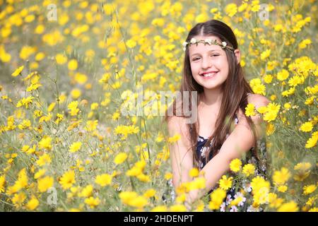 Junge 11 Jahre alte Mädchen in floralen Sommerkleid in einem Feld von gelben wilden Gänseblümchen Stockfoto