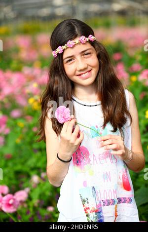 Junges Mädchen von 12 Jahren in weißem Kleid in einem Treibhaus aus rosa Blumen Stockfoto