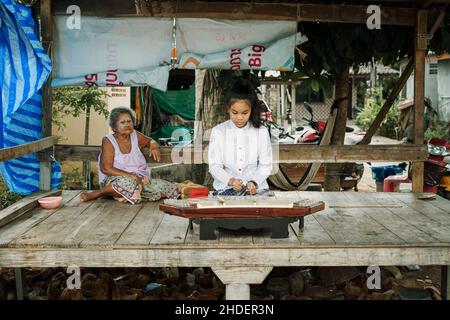 Ein wunderschönes thailändisches Mädchen, das Khim, das traditionelle thailändische Musikinstrument in der Nähe der Großmutter, im Freien auf einer Holzplatte spielt. Freizeit- und Hobbykonzept. Stockfoto