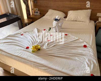 Dekoration von Elefantenhandtüchern und roten Rosenblättern auf weißem Bett im hellen Hotelzimmer im Delphin Imperial Hotel, Kundu, Aksu, Türkische Riviera, Provinz A Stockfoto