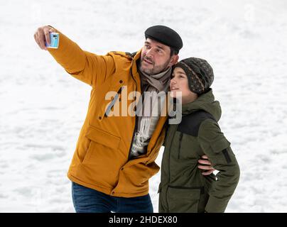 Vater und Sohn machen während der Winterferien Selfie auf Schnee im Park Stockfoto