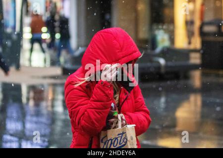 Frau in rotem Anorak hält Kapuze in Regen, Schnee und Schneeschauern an einem kalten Tag für Käufer im Stadtzentrum als Temperatur sinkt . Southport, Merseyside. Wetter in Großbritannien. 6. Januar 2022. Kredit; MediaWorld/Bilder/AlamyLiveNews Stockfoto