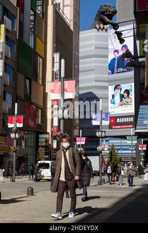 Ein Japaner, der eine OP-Maske gegen COVID-19 trägt, geht mit einem großen Godzilla-Modell auf der Hotel Gracery hinter dem Kabukicho-Distrikt spazieren. Stockfoto