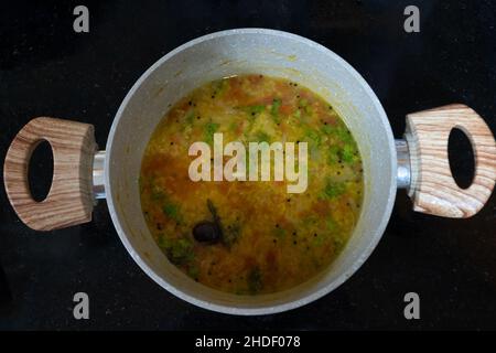 Draufsicht auf die Linsensuppe mit Zutaten in einem Kochgefäß auf einer glänzenden schwarzen Marmorplatte. Gesunde vegetarische Suppe. Stockfoto