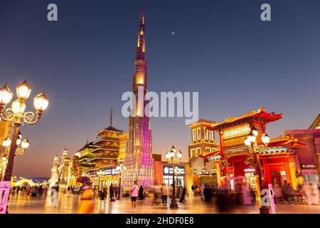 Dubai, VAE, 10.01.21. Global Village Vergnügungspark bei Nacht mit beleuchteten Burj Khalifa Miniatur und Pagoden, Halbmond am Himmel, Menschen. Stockfoto