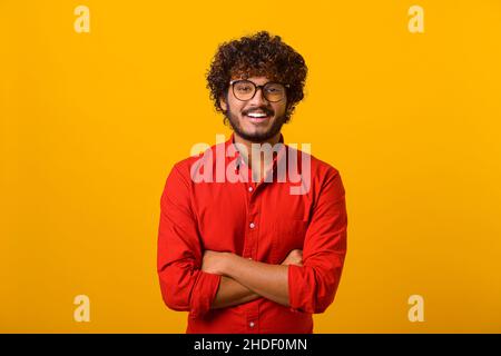 Porträt eines bärtig aussehenden Mannes mit schwarzer Brille im lässigen Stil, der die Kamera anschaut und lächelt. Studio auf orangefarbenem Hintergrund aufgenommen Stockfoto