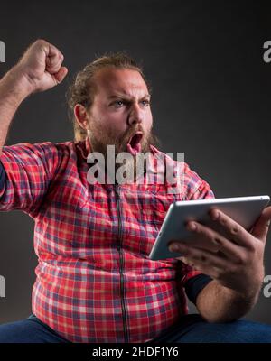 Studioaufnahme eines jungen bärtigen Mannes, der über das Touchpad gute Nachrichten feierte. Stockfoto
