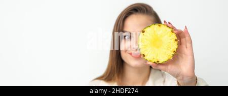 Eine junge, attraktive, hübsche, kaukasisch lächelnde Frau hält eine Ringschneide-Ananas, die ihr Auge vor einem weißen Hintergrund bedeckt. Gesunde Ernährung Konzept Stockfoto