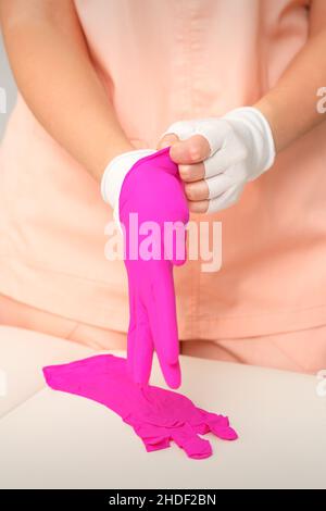 Die Hände der Kosmetikerin tragen die rosa Gummihandschuhe an, um die Kunden zu empfangen Stockfoto