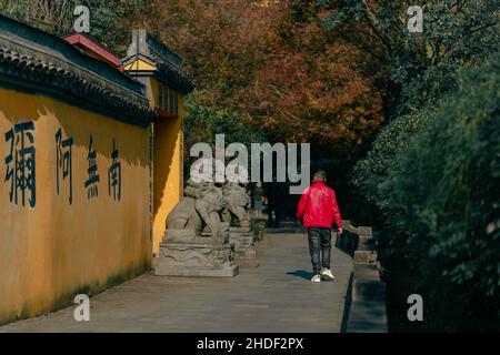 Mann in einer roten Jacke, der in der Nähe eines Tempels in Hangzhou, China, herumläuft Stockfoto