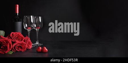 Valentinstag-Banner mit Rotwein, Strauß roter Rosen auf schwarzem Hintergrund. Einladung oder Grußkarte. Speicherplatz kopieren. Stockfoto