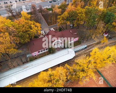 Schauen Sie hinunter auf den Children's Southern Railway Station. Gleislinie und Bahnsteig mit Zug in leuchtend gelben Herbstbäumen. Luftaufnahme von der Baumkrone auf dem farbenfrohen Kha Stockfoto