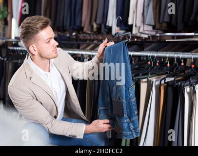 Männlicher Kunde, der Hosen im Geschäft für Männertücher untersucht Stockfoto