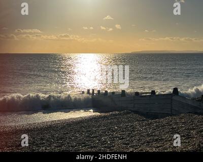 Sonnenlicht spiegelte sich über dem Meer, als Wellen am Strand von Hayling Island, Hampshire, Großbritannien, eine Groyne umspülten Stockfoto