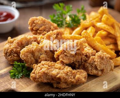 Knusprig gebratene Hähnchengerichte und pommes frites, garniert mit Petersilie auf einem hölzernen Schneidebrett Stockfoto