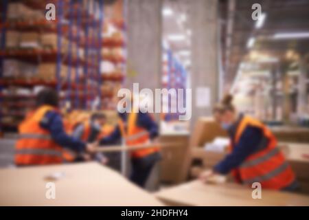 Verwischen Sie den Lagerhintergrund. Lagerarbeiter, der in einem großen Lager in einem großen Lager Paket im Regal nimmt Stockfoto
