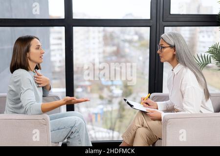 Frustrierte junge Patientin, die während der Therapiesitzung mit einer Psychotherapeutin über Probleme und Ängste spricht. Konzept der psychischen Gesundheit Stockfoto