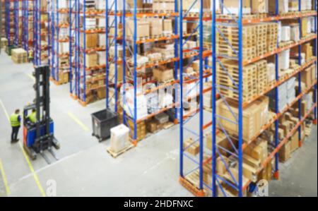 Verwischen Sie den Lagerhintergrund. Ansicht von oben, wie Lagerarbeiter Waren umziehen und Lagerbestände im Gang zwischen Reihen hoher Regale voller verpackter Boxen zählen Stockfoto