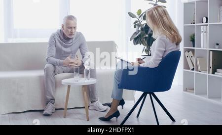 Reifer Sportler und blonde Psychologin, die im Sprechzimmer miteinander sprechen Stockfoto