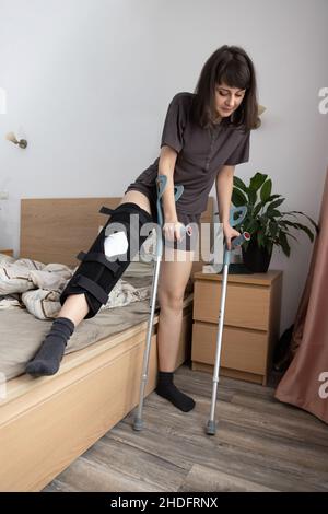 Junge Frau, die nach einer ACL-Operation versucht, aus dem Bett aufzustehen. Stockfoto