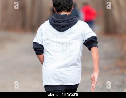 Rückansicht einer Nahaufnahme eines Gymnasiasten, der während des Trainings einen kleinen Hügel auf einem unbefestigten Pfad im Wald hochläuft. Stockfoto