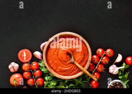 Hausgemachte Tomatensauce in Holzschüssel auf dunklem Steingrund mit Platz zum Kopieren. Draufsicht, flach liegend Stockfoto