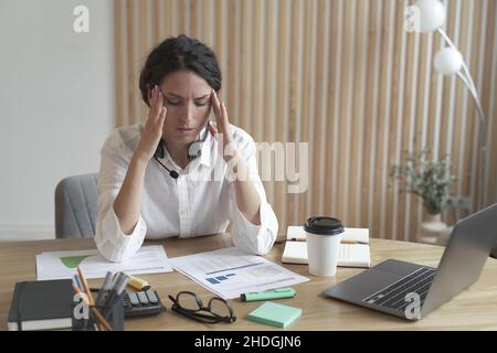 Frustriert verärgert italienerin, die den Kopf in den Händen hält und nach einem harten Arbeitstag Kopfschmerzen hat Stockfoto
