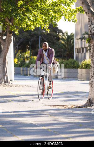 afroamerikanischer Geschäftsmann, der auf der Straße auf dem Weg zum Büro ein Fahrrad fährt Stockfoto