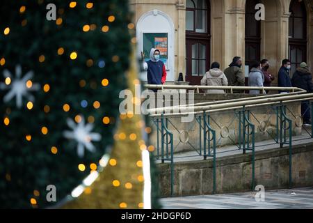 Am Weihnachtstag in London stehen Menschen hinter Weihnachtsdekorationen vor einem Impfzentrum. Stockfoto