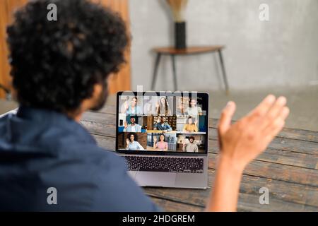 Männlicher Mitarbeiter beteiligte sich an einem Videotreffen auf dem Laptop mit einem unterschiedlichen Arbeitsteam, indischer Mann, der Computer-App für Videoverbindungen mit verschiedenen Kollegen verwendete, Brainstorming online, Handwinken, Videomeeting mit der Hand Stockfoto