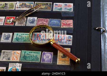 Stempelzange und eine Lupe auf einem Briefmarkenbinder, gefüllt mit alten US-Marken. Stockfoto