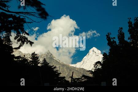 Majestätischer himalaya-Berg Mt sudarshan bedeckt mit Schnee. Silhouettierte Baumlinie im Vordergrund. Blauer Himmel und treibenden Wolken. Tagesaufnahme Stockfoto