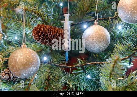 Coronavirus-Pandemie - Eine Covid-19 Booster-Impfstoff-Spritze, die an einem Weihnachtsbaum hängt Stockfoto