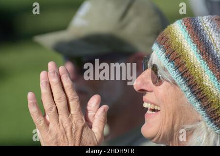 Die ältere, grauende Frau aus den 60ern mit Sonnenbrille und handgestrickter, warmer Strickmütze, die sich Sorgen macht, sich aber darüber freut, wie es ihrem Enkelkind im Fußballspiel geht Stockfoto