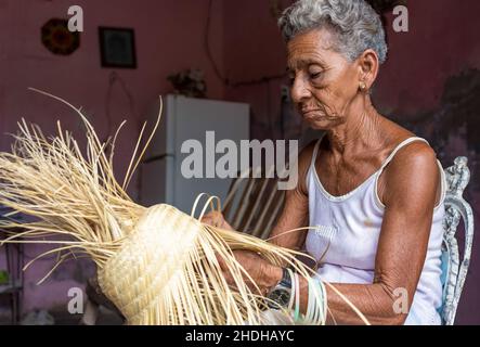 Porträt einer älteren afro-karibischen Frau, die einen Strohhut macht, der ein traditionelles Souvenir ist. Sie arbeitet im Wohnzimmer ihres Hauses. Januar 6, Stockfoto