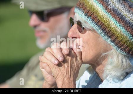Die ältere, grauende Frau aus den 60ern mit Sonnenbrille und handgestrickter, warmer Strickmütze, die sich Sorgen macht, sich aber darüber freut, wie es ihrem Enkelkind im Fußballspiel geht Stockfoto