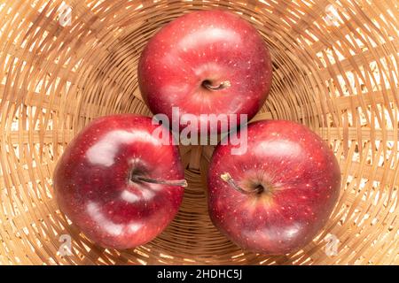 Drei reife rote Äpfel in einer Strohschale, Nahaufnahme, Draufsicht. Stockfoto
