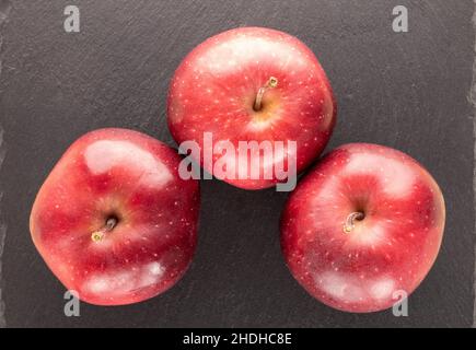 Drei reife rote Äpfel auf einem Schieferstein, Nahaufnahme, Draufsicht. Stockfoto