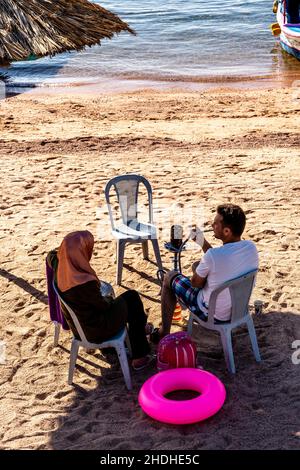 Ein Paar sitzt am öffentlichen Strand in Aqaba, im jordanischen Aqaba. Stockfoto