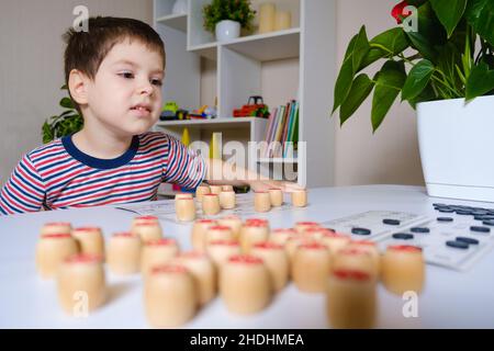 Ein 4-jähriger Junge spielt loto und studiert Zahlen anhand eines Brettspiels. Stockfoto